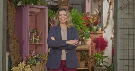 Portrait of a businesswoman owner of local shop with arms crossed smiling at camera. One middle aged female entrepreneur smiling at camera standing in front of sidewalk store