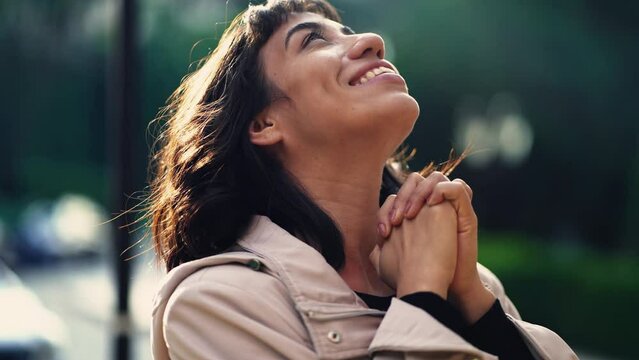 A grateful hispanic woman praying to God with hands clenched looking at sky smiling. Spiritual person having HOPE