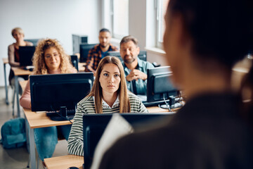 Mid adult woman attending computer class lecture in classroom.