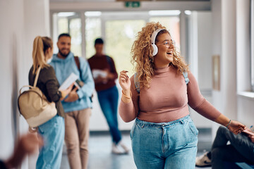 Cheerful female student listens music over headphones while walking through hallway.