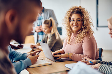 Young happy woman using laptop during class at university and looking at camera.