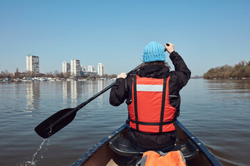 Obraz premium Man paddling in a canoe on a Danube river in urban area, small recreational escape, hobbies and sports outdoors.