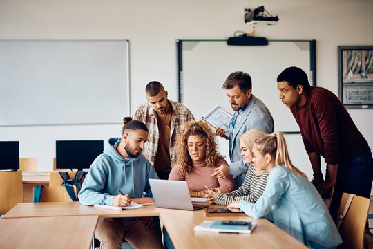 University Teacher And His Students Using Laptop In Classroom.