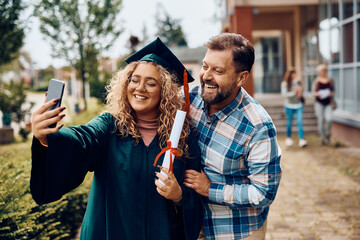 Happy student taking selfie with her father on her graduation day.