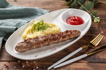 Grilled sausage with herb potatoes and ketchup, tasty summer picnic dish, on a dark wooden background