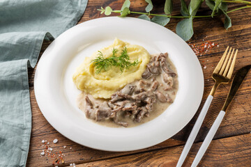 Stew with meat mushrooms and mushed potatoes on white plate. Wooden background.