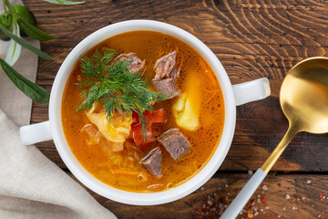 Meat and vegetables soup with parsley in bowl over rustic wooden background close up
