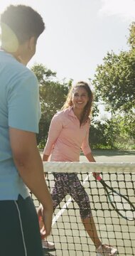 Vertical video of happy biracial woman and man with tennis rackets