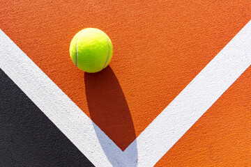Yellow tennis ball on new orange outdoor tennis court with white baseline and black out of bounds	