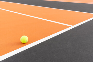 Yellow tennis ball at orange tennis court with white baseline and black out of bounds	