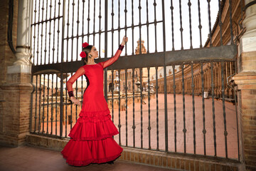 Young teenage woman in red dance suit with ruffles and red carnations in her hair doing flamenco...