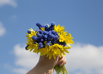 hand holds a bouquet of blue and yellow flowers against the sky. Stand with Ukraine. Gratitude for...
