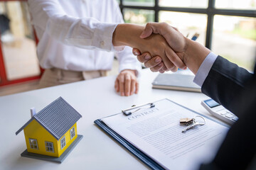 The estate agent and client are shaking hands after a good deal home loan after discussing and signing a contract to rent a house with an approved insurance form