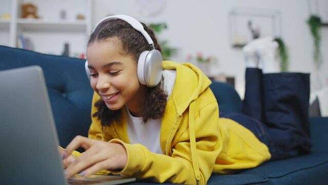 Black teenage girl in headphones listening to favorite song on laptop, music app