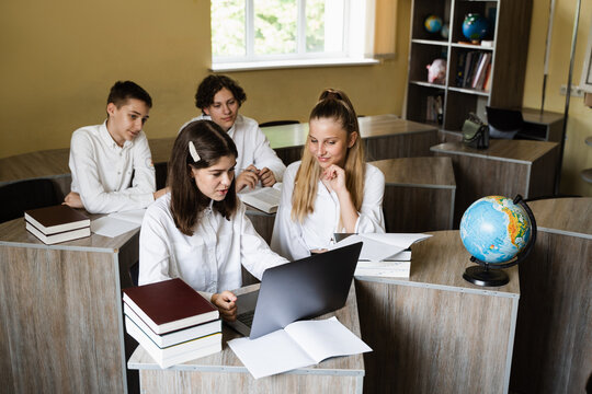 Children in school at geography lesson with globe study online on laptop and discuss different countries. Education concept. Pupils at school communicating with classmates online.