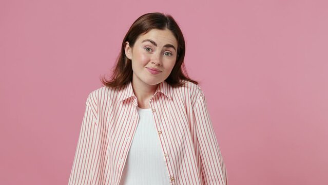Young woman she wear shirt t-shirt shrugging shoulders looking puzzled have no idea nothing to say standing questioned and unaware I don't know why isolated on plain pastel light pink background