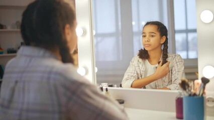 Upset African American teenage girl looking in mirror and feeling insecure