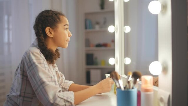 African American teen girl applying lipstick in front of mirror, beauty routine