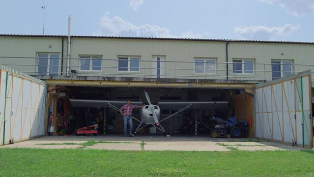 Aviator standing airplane hangar countryside. Pilot man posing near plane.