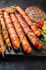 Traditional Grillplatte mit Bratwurst, Hamburger und Speck Grillfackel zubereitet für eine Sommer Grillparty serviert als close-up auf einem rustikalen Board 