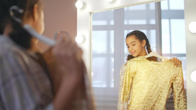 Beautiful black schoolgirl trying on prom dress in front of mirror, confidence
