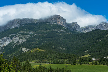 Vercors mountains under clouds in Die region with green land and farms underneath
