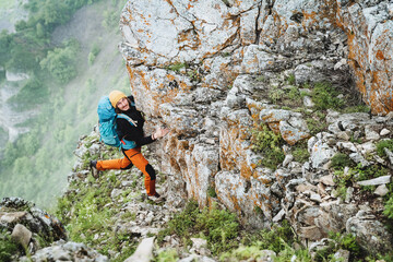 The climber climbs the rock up with a heavy backpack on his back, the adrenaline sport is extreme, the mountain peak will be conquered by a person, clinging to the stone with his hand.
