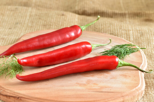 In the picture, three red chili peppers lie on a cutting board.