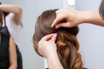 Fototapeta premium The hairdresser makes a hairstyle to a young attractive woman with a beautiful make-up in a black dress in a beauty salon.