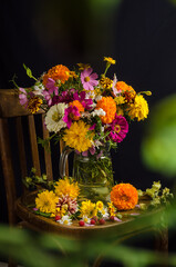 Gorgeous summer still life with a bouquet of multi-colored garden and wild flowers on a black background with a blurred bokeh of greenery