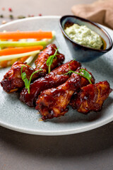 chicken wings in barbecue sauce on plate with blue cheese sauce macro close up on brown stone table vertical