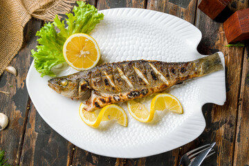 Fried sea bass with sliced lemon on white plate on old wooden table