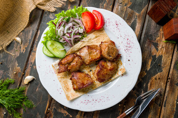Kebab of pork with red onion and sliced vegetables on old wooden table top view