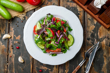 Vegetable salad with tomatoes and cucumbers with red onion top view on old wooden table