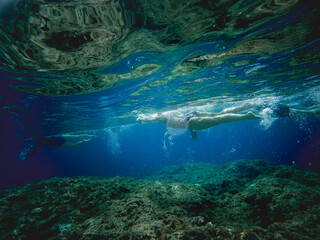 underwater image with crystal clear sea and people swimming on the surface