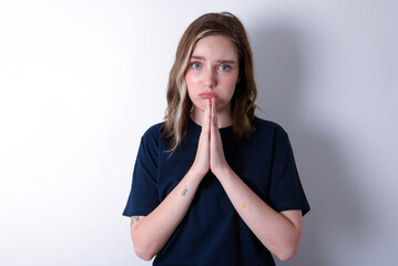 Positive young caucasian woman wearing black T-shirt over white background smiles happily, glad to receive pleasant news from interlocutor, keeps palms together, People emotions concept.