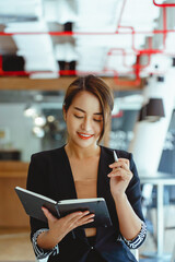 Young business woman sitting at table and taking notes in notebook.