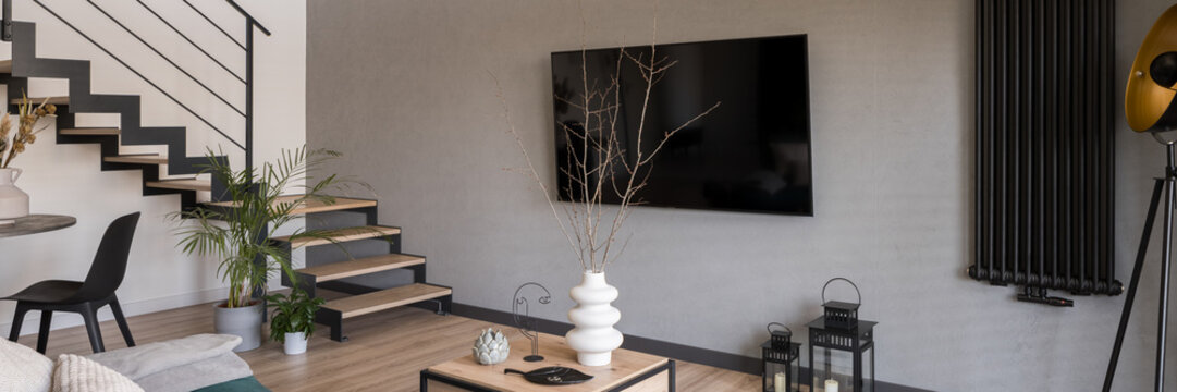 Big tv on concrete wall in living room with stairs, panorama