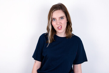 Portrait of dissatisfied young caucasian woman wearing black T-shirt over white background smirks face, purses lips and looks with annoyance at camera, discontent hearing something unpleasant