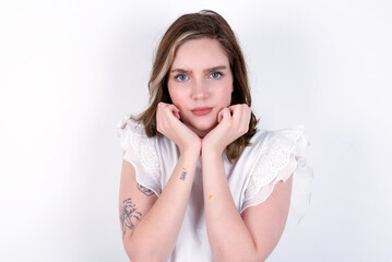 Portrait of sad young caucasian woman wearing white T-shirt over white background hands face