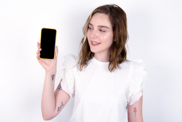 Fototapeta premium Photo of interested young caucasian woman wearing white T-shirt over white background hold telephone look side empty space screen