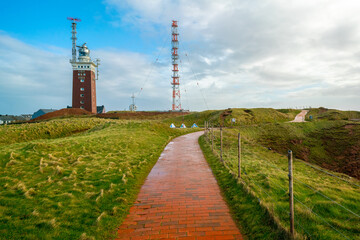Golden hour by the lighthouse on the Heligoland, or Helgoland island, Germany. Cloudy sky and paved...