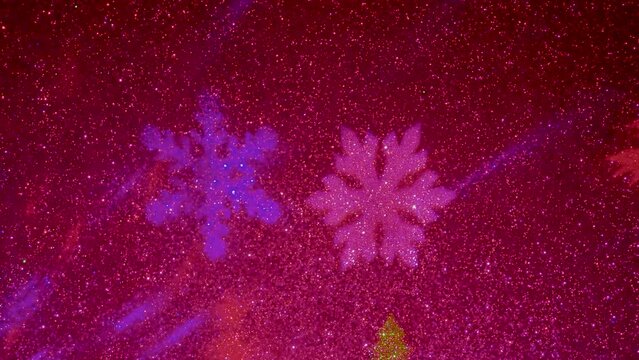 Christmas background. On a flashing background of a red hue, images of Christmas trees in red and green colors and snowflakes in blue and red fly. Flashing background with rays of light