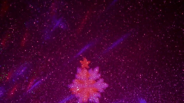 A carousel of light beams of different colors is set against a constantly flashing background that changes colors. Flying colored silhouettes of Christmas trees and snowflakes.