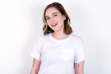 Fototapeta premium young caucasian woman wearing white T-shirt over white background with broad smile, shows white teeth, feeling confident rejoices having day off.