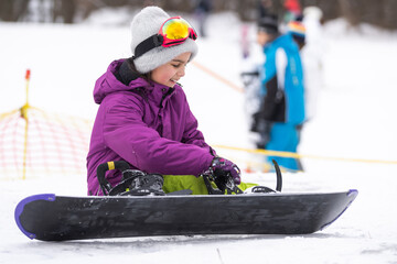 little cute girl learning to ride a children's snowboard, winter sports for the child, safety of...