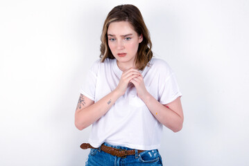 Sad young caucasian woman wearing white T-shirt over white background feeling upset while spending time at home alone staring at camera with unhappy or regretful look.