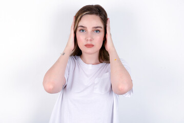 Frustrated young caucasian woman wearing white T-shirt over white background plugging ears with hands does not wanting to listen hard rock, noise or loud music.