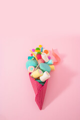 Creative junk food concept of a lots of delicious sweets in an ice cream cone on pastel pink...