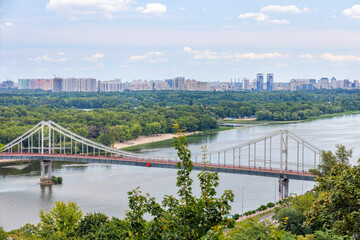 Beautiful cityscape of Kyiv with a view of the mountain slope, the Dnipro river with a footbridge.